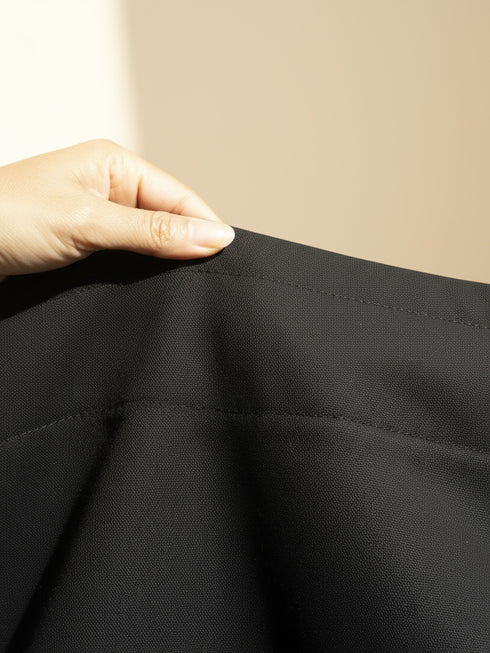 Close-up of a hand touching black fabric against a beige background